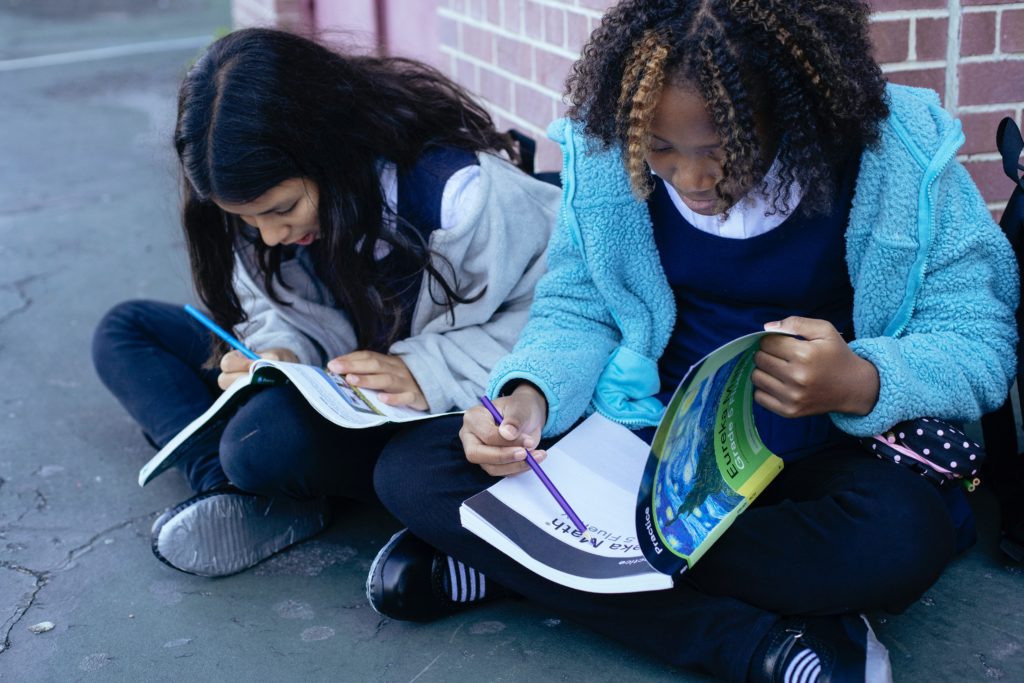 Two students sitting on playground in uniforms with books open