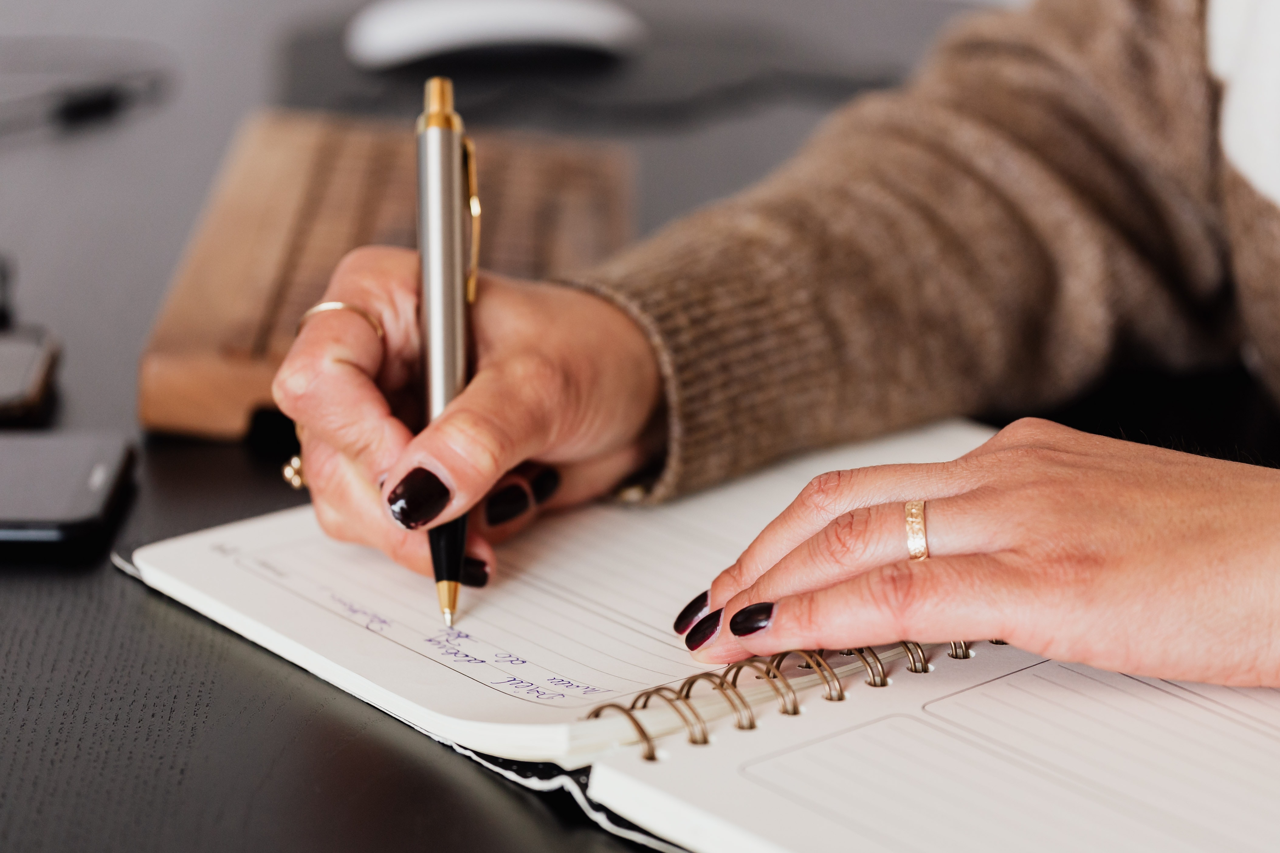 Woman with pen in right hand writing in notebook